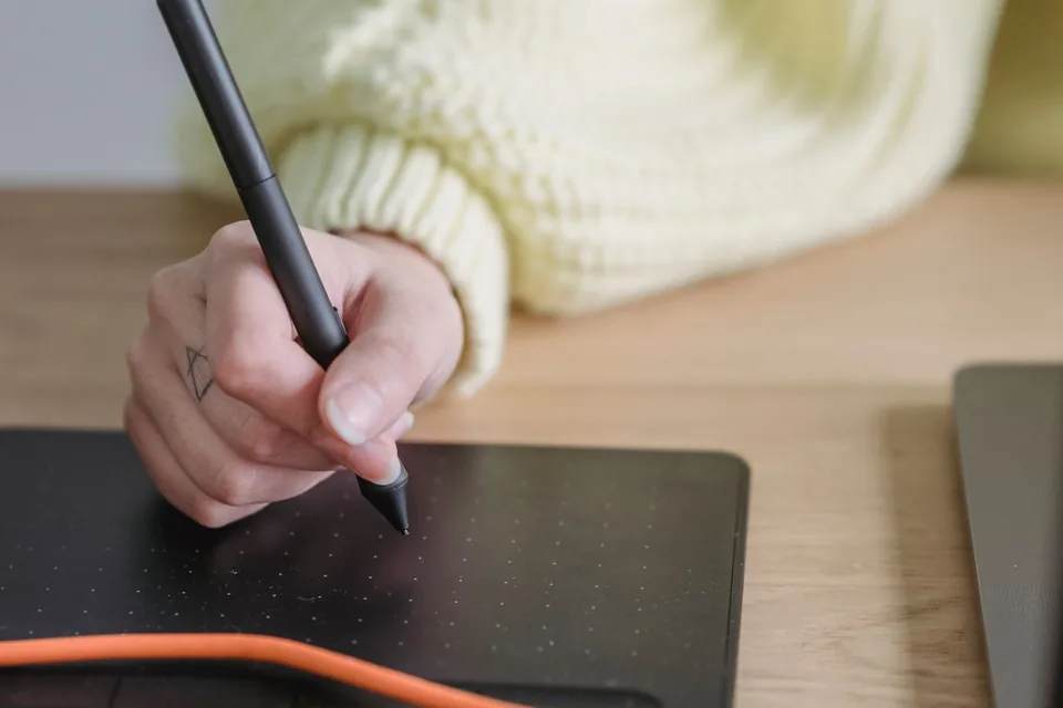 Artist using a stylus on a drawing tablet beside a laptop