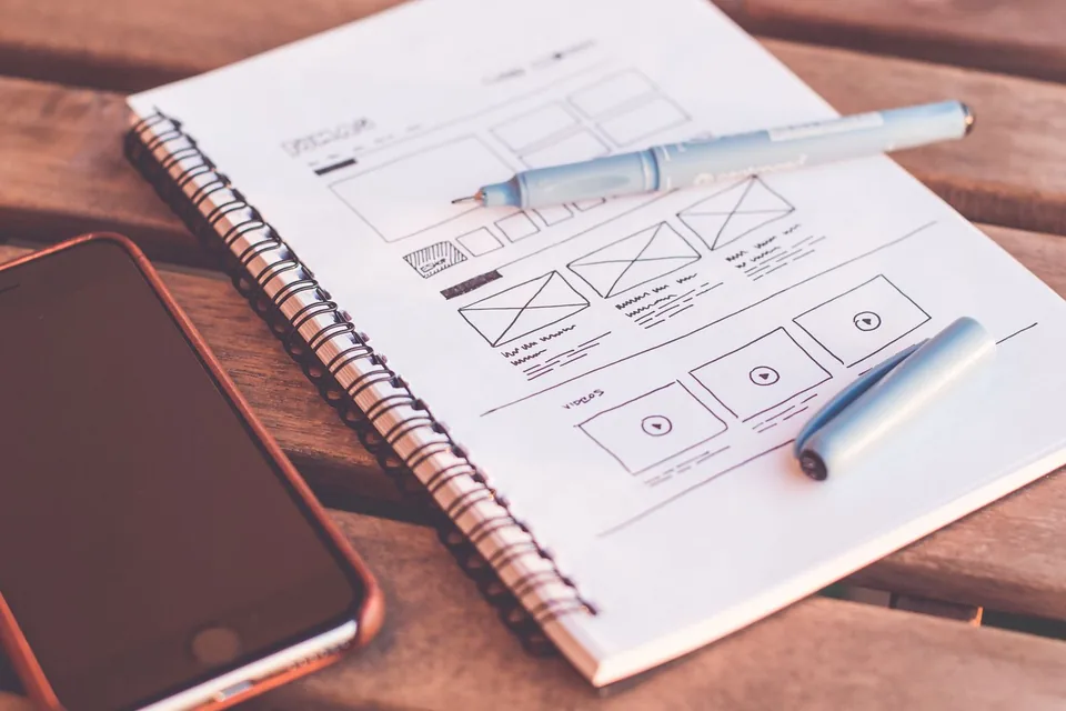 Notebook with hand-drawn interface wireframes beside a phone