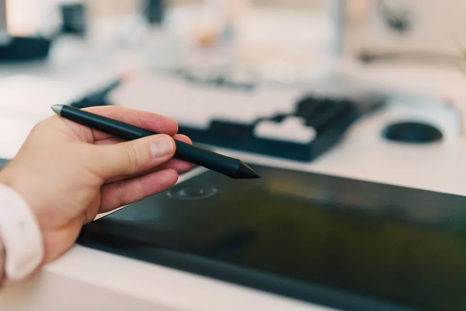 Hand holding a stylus above a black graphics tablet